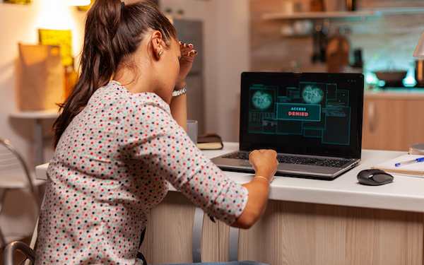 Ein Mädchen sitzt mit dem Rücken zur Kamera an einem Schreibtisch auf dem ein aufgeklappter Laptop steht und hat ihren Kopf in die linke Hand gestützt.