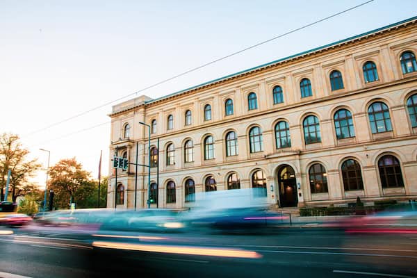 Foto enes Gebräudes, davor ist eine Straße zu sehen mit Autos in Langzeitbelichtung, die nur als Schlieren zu sehen sind.