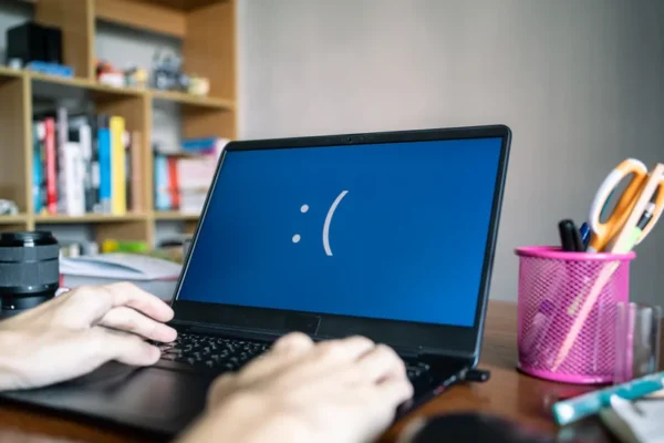 Aufgeklappter Laptop steht auf Tisch. Auf dem Bildschirm ist ein mit Doppelpunkt und offener Klammer getippter unzufriedener Smiley zu sehen.