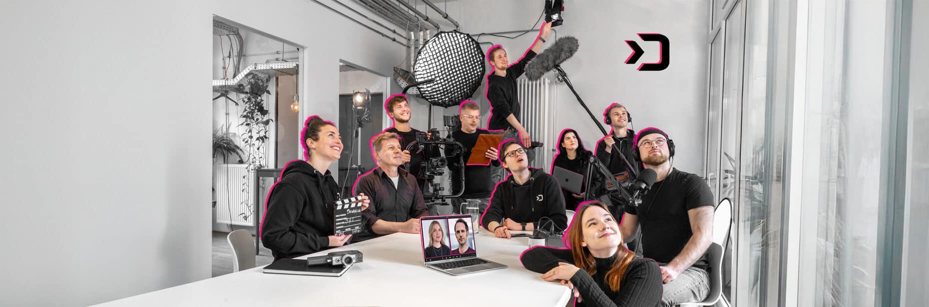 Eine Gruppe von Menschen ist um einen Tisch herum aufgereiht und schaut seitlich aus dem Foto heraus in eine Kamera.