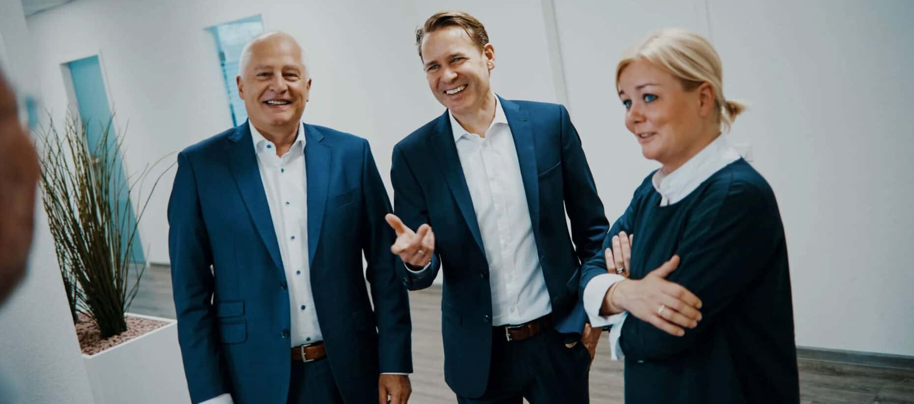 Drei Menschen stehen im Gespräch nebeneinander und schauen vorbei an der Kamera in die selbe Richtung seitlich aus dem Bild.