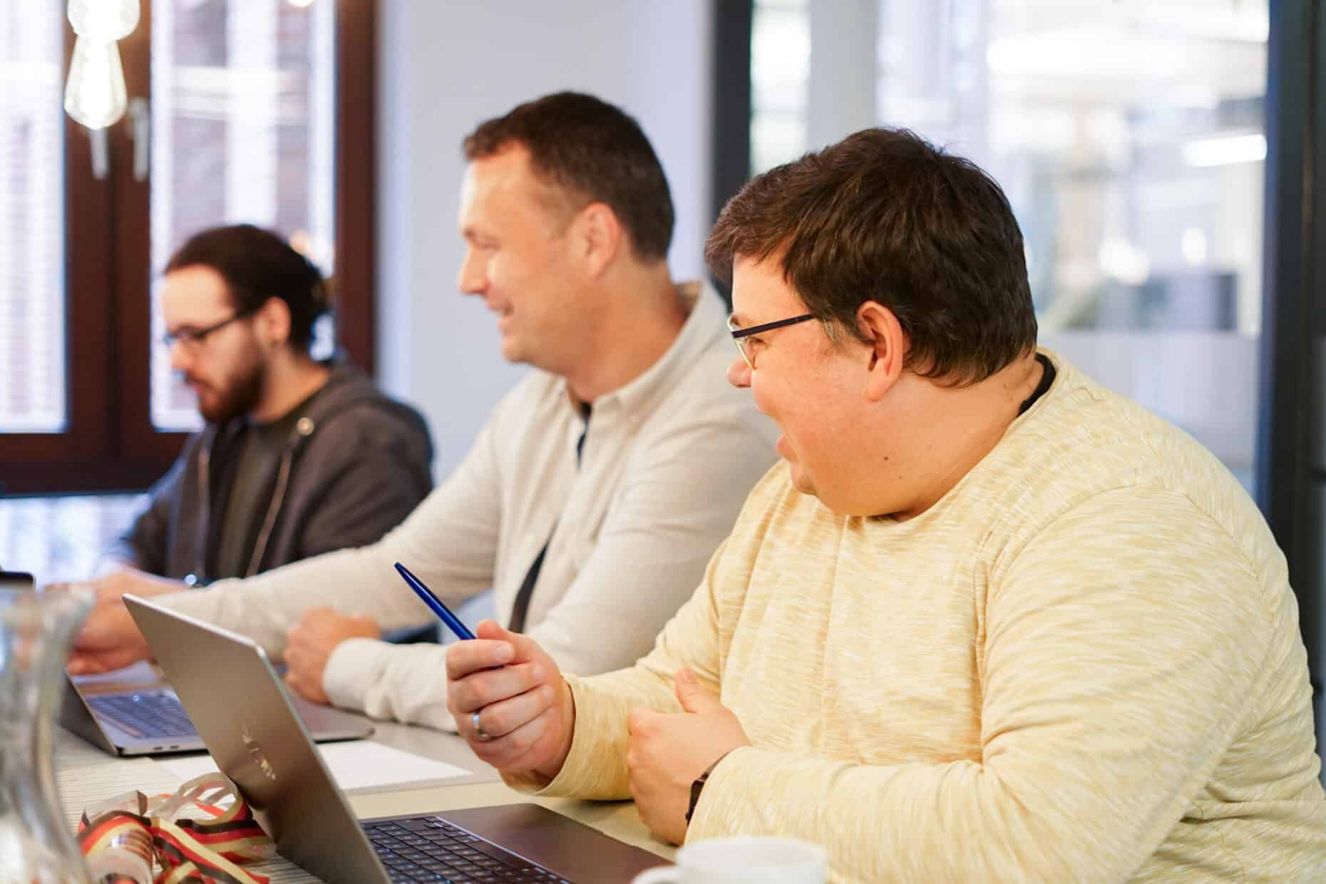 Drei Männer, die an einem Tisch mit Laptops sitzen.