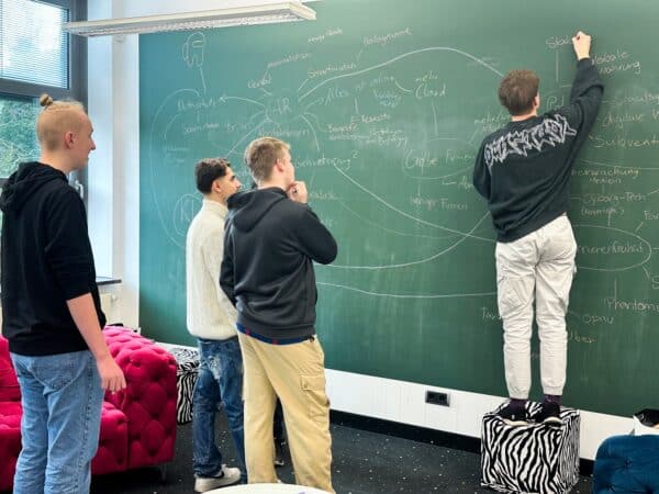 Vier junge Männer stehen vor einer großen Tafel und schreiben Begriffe auf diese.