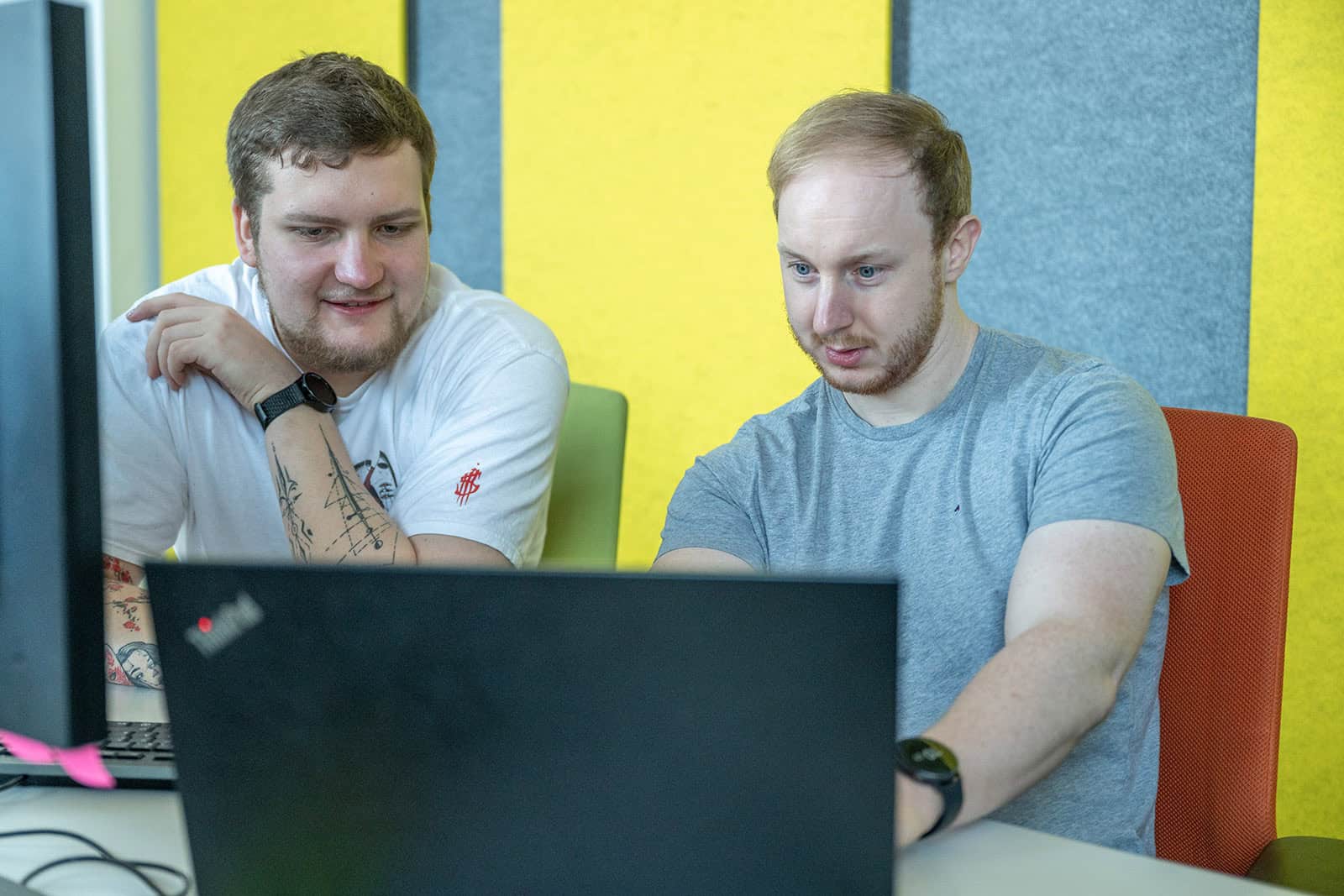 Zwei Männer sitzen vor einem Laptop und schauen auf den Bildschirm.