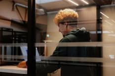 Ein Mann steht hinter einer Glasscheibe an einem Laptop.