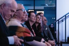 Seitliche Aufnahme eines Publikums was auf eine Bühne schaut.