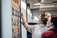 Zwei Frauen stehen vor einer Pinnwand mit Post-Its.