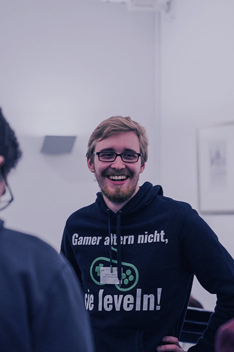 Ein Mann lächelt in die Kamera und stützt dabei seine Hände in die Hüfte.