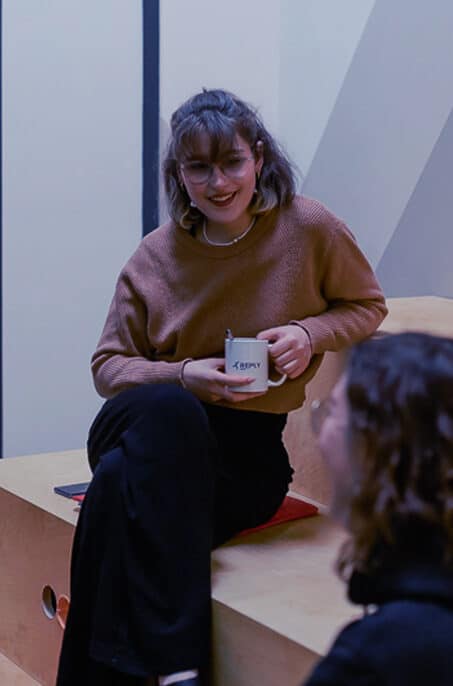 Eine Frau sitzt auf einem Tritt und hat eine Kaffeetasse in der Hand.