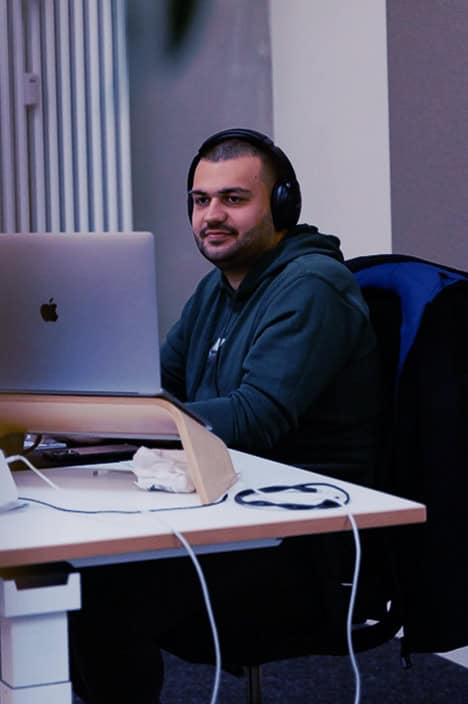 Ein Mann sitzt an einem Schreibtisch mit einem Laptop und hat Kopfhörer auf.