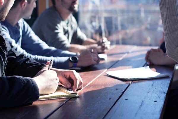 Mehrere Personen sitzen an einem Tisch mit Blöcken und Stiften.