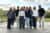 Neun Menschen stehen draußen im Freien für ein Gruppenfoto zusammen und schauen freundlich in die Kamera.