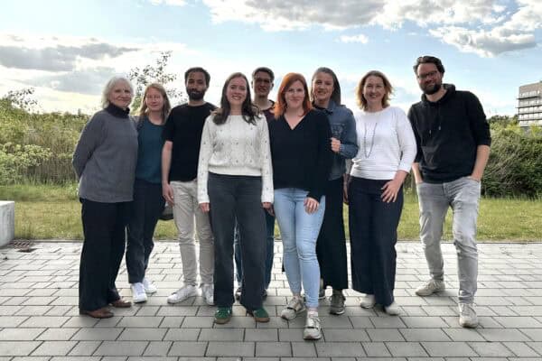 Neun Menschen stehen draußen im Freien für ein Gruppenfoto zusammen und schauen freundlich in die Kamera.