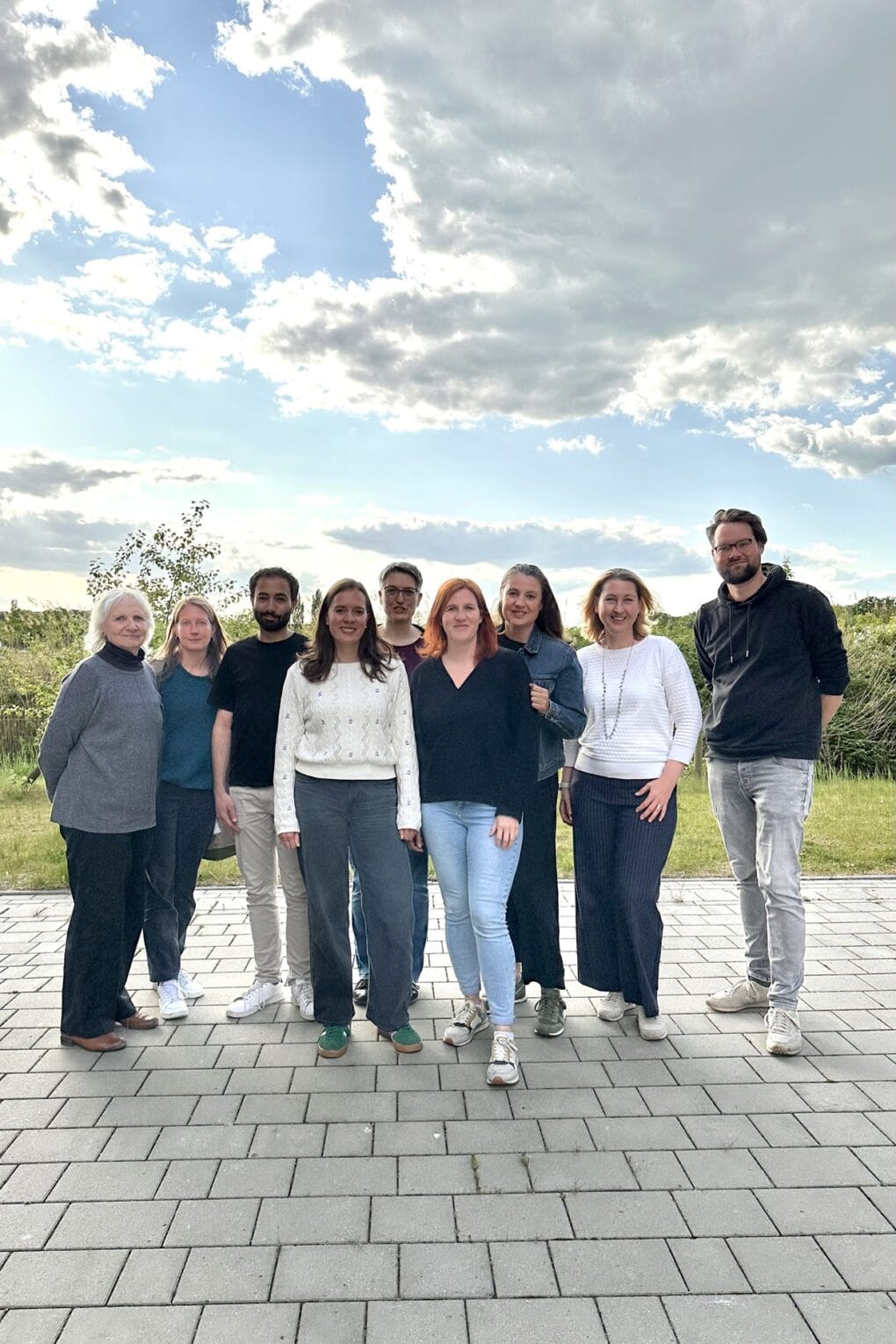 Neun Menschen stehen draußen im Freien für ein Gruppenfoto zusammen und schauen freundlich in die Kamera.
