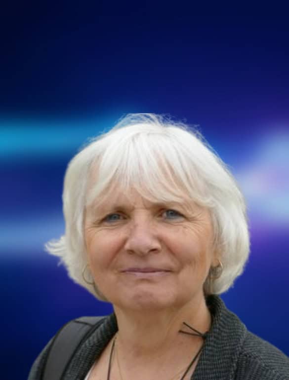 Portrait einer Person, die freundlich in die Kamera guckt. Der dunkelblau-liafarben und verschwommene Hintergrund ist in der Bildberarbeitung nachträglich hinzugefügt worden.