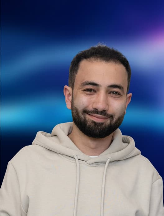 Portrait einer Person, die freundlich in die Kamera guckt. Der dunkelblau-liafarben und verschwommene Hintergrund ist in der Bildberarbeitung nachträglich hinzugefügt worden.