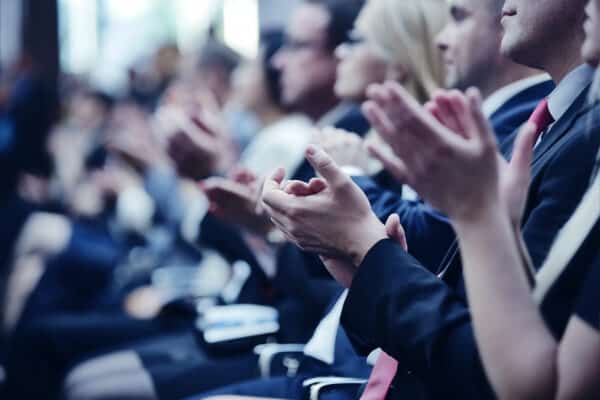 Nahaufnahme in einer Reihe sitzender Menschen. Der Fokus liegt auf den klatschenden Händen.