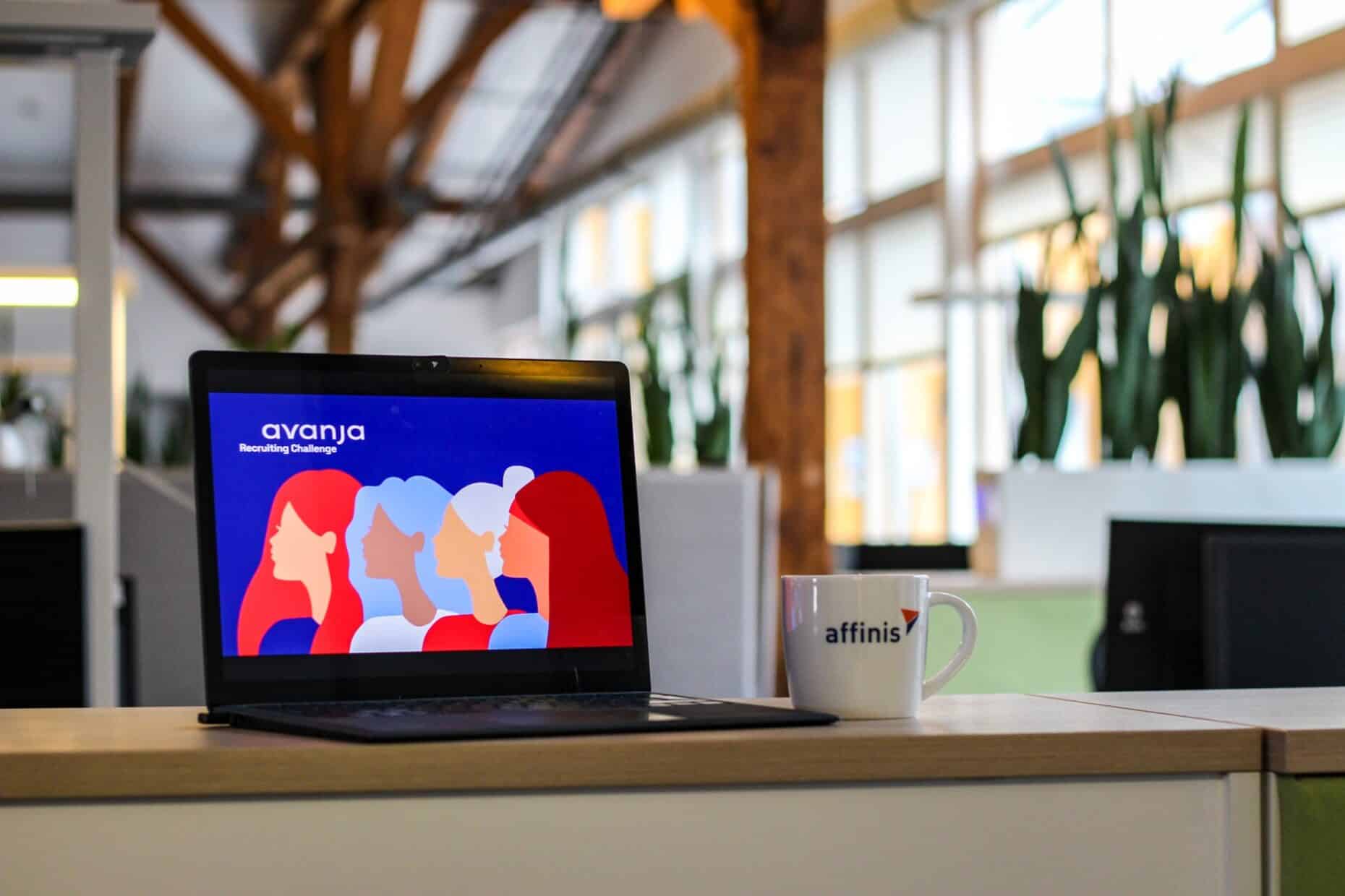 Auf einem im Bildauscchnitt angeschnittenen Tisch steht ein aufgeklappter Laptop. Darauf ist eine Illustration von vier Frauenöpfen, darüer steht 