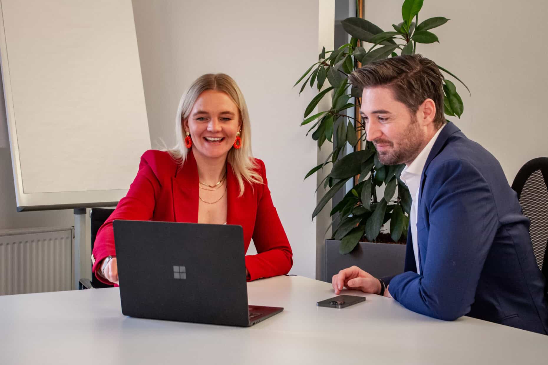 Eine Frau und ein Mann sitzen an einem Konferenztisch vor einem Laptop.